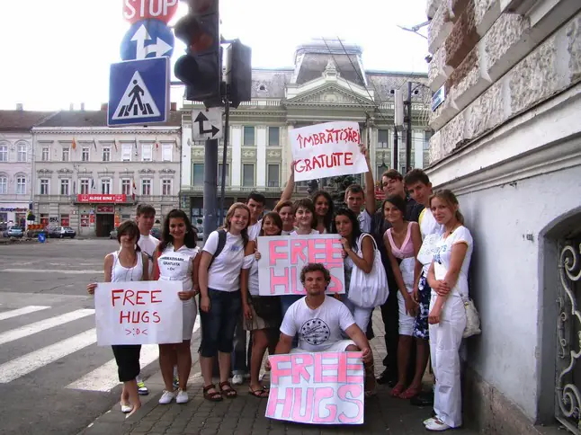 Grup de liceeni pe un trotuar din centrul Aradului, cu pancarte Free Hugs și Îmbrățișări gratuite