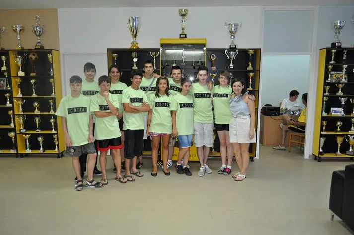 Grup de tineri voluntari în tricouri verzi, într-o sală cu cupe sportive
